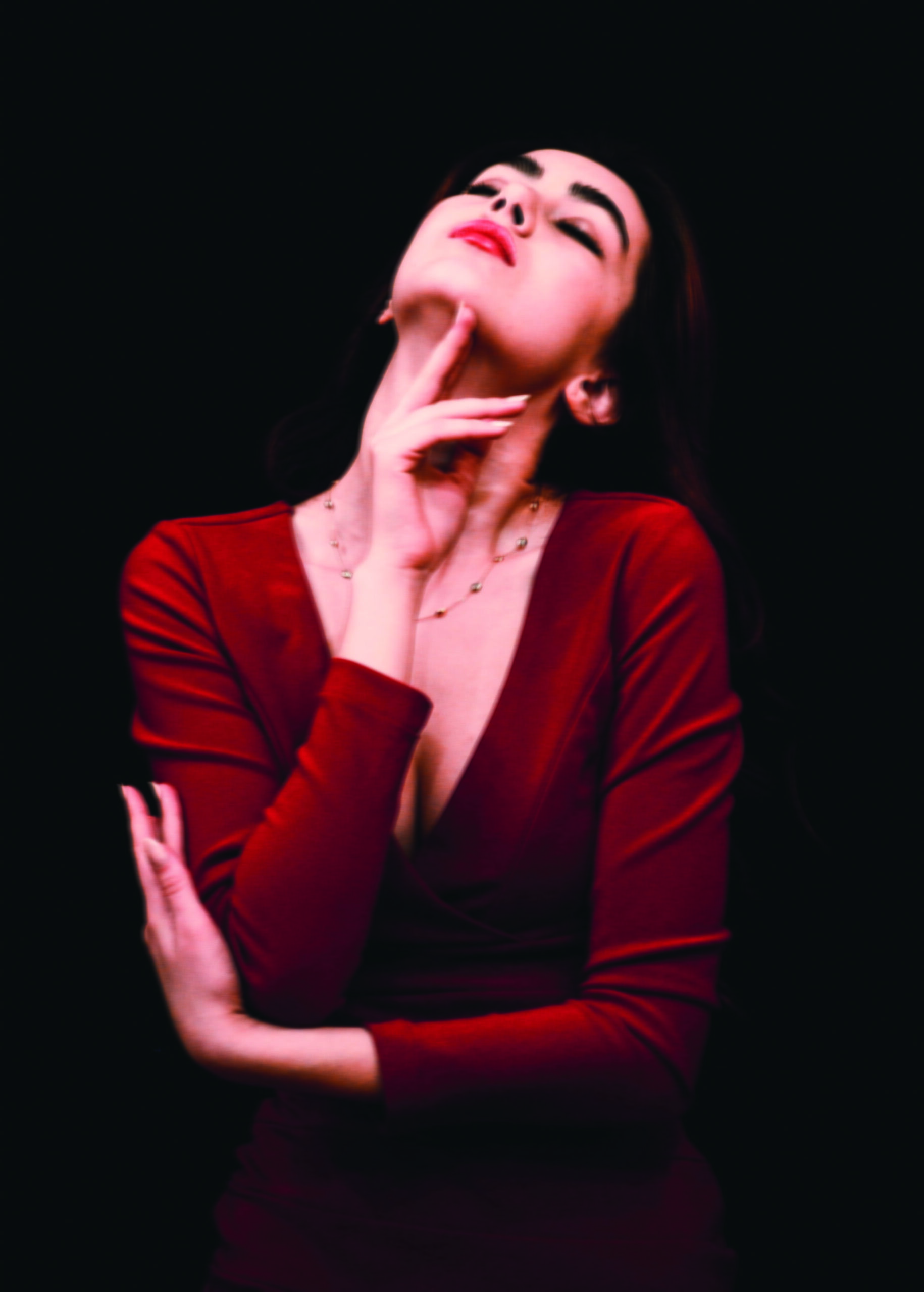 Das Bild zeigt eine nachdenkliche Frau in einem roten Kleid. Sie hat ihren Kopf nach hinten gelegt und berührt mit ihrer rechten Hand ihr Kinn. Die Augen sind geschlossen.